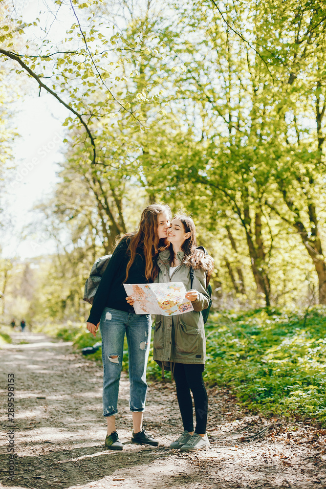 Two girls standing in a autumn forest. Friends have fun in a park. Tourists use the map.