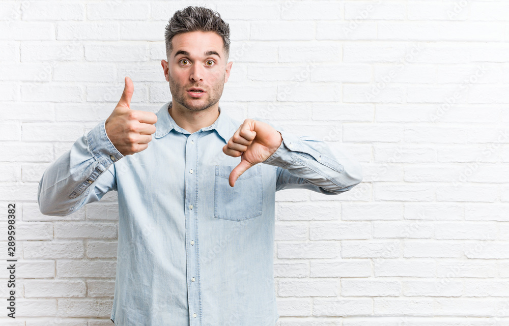 Young handsome man against a bricks wall showing thumbs up and thumbs down, difficult choose concept Young handsome man against a bricks wall showing thumbs up and thumbs down, difficult choose concept