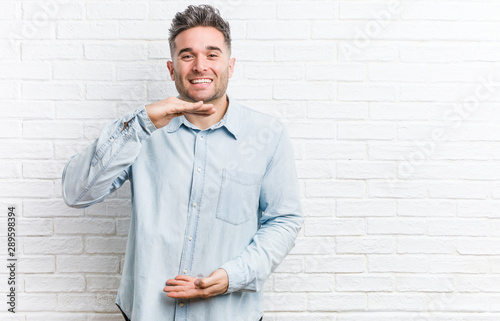 Young handsome man against a bricks wall holding something with both hands, product presentation.