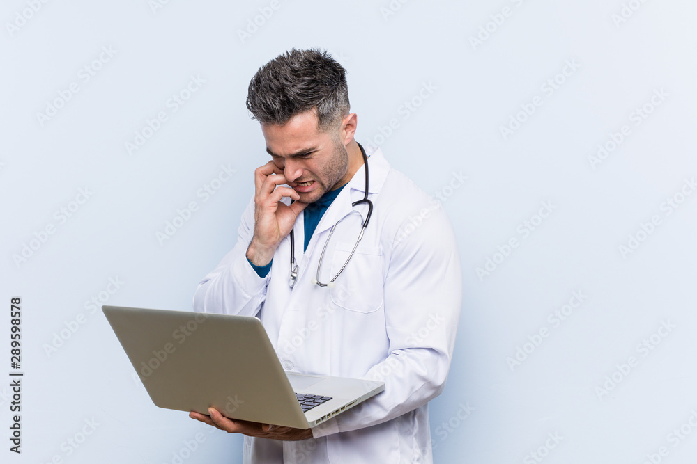 Caucasian doctor man holding a laptop biting fingernails, nervous and very anxious. Caucasian doctor man holding a laptop biting fingernails, nervous and very anxious.