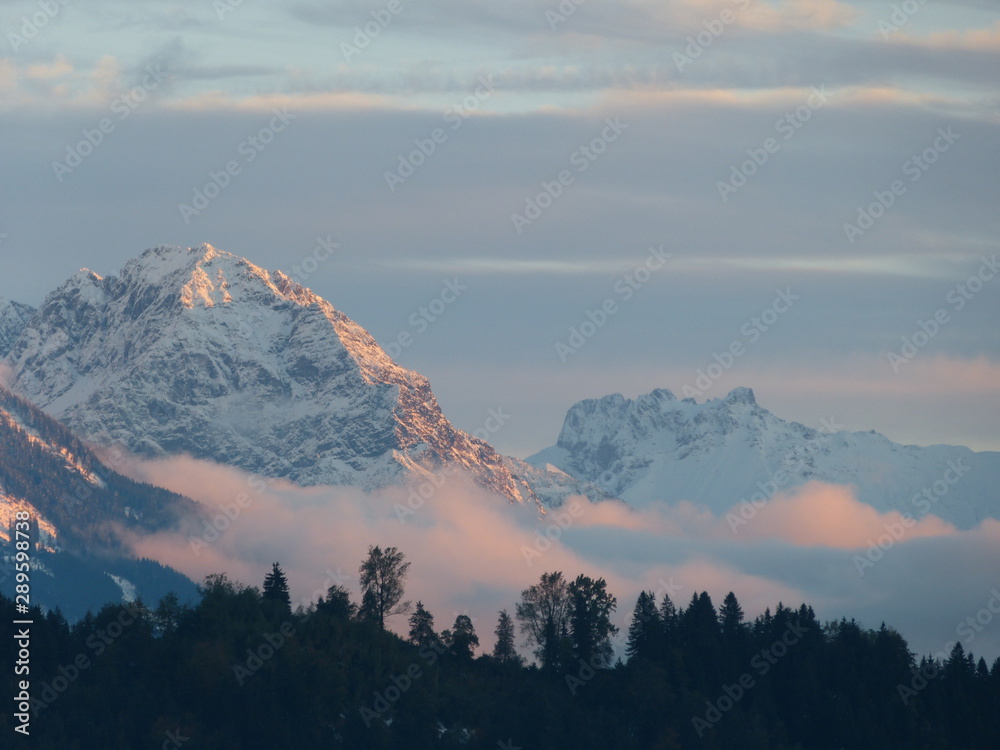 Obraz premium sunset in snowy mountains with low level clouds and black forest silhouette