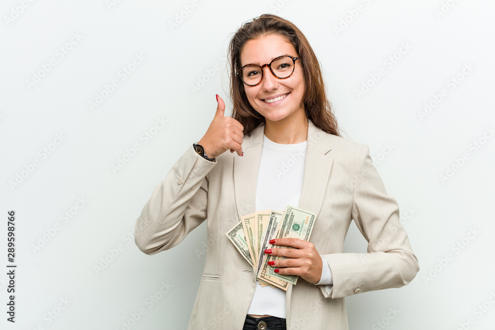 Young european business woman holding dollar banknotes smiling and raising thumb up Young european business woman holding dollar banknotes smiling and raising thumb up