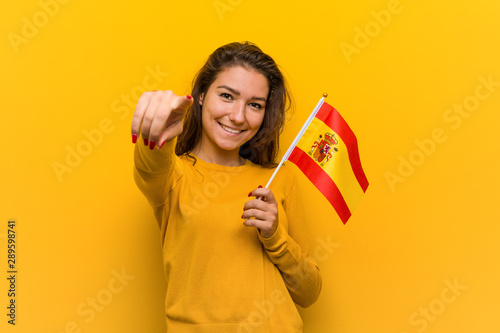Young european woman holding a spanish flag cheerful smiles pointing to front. photo