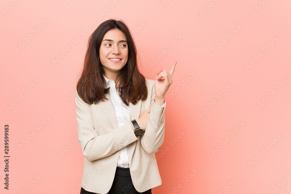 Young brunette business woman against a pink background smiling cheerfully pointing with forefinger away. Young brunette business woman against a pink background smiling cheerfully pointing with forefinger away.