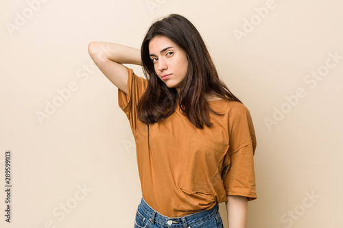 Young brunette woman against a beige background suffering neck pain due to sedentary lifestyle.