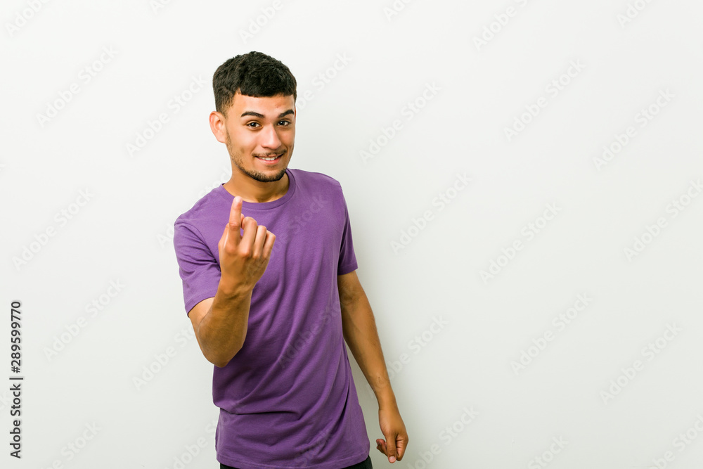 Young hispanic man pointing with finger at you as if inviting come closer.