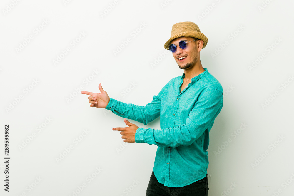 Young hispanic man wearing a summer clothes excited pointing with forefingers away.