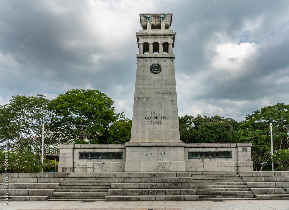 Singapore - March 20, 2019: Gray stone Cenotaph war memorial surrounded by green foliage in Esplanade Park under heavy gray sky promising rain. World War One side.