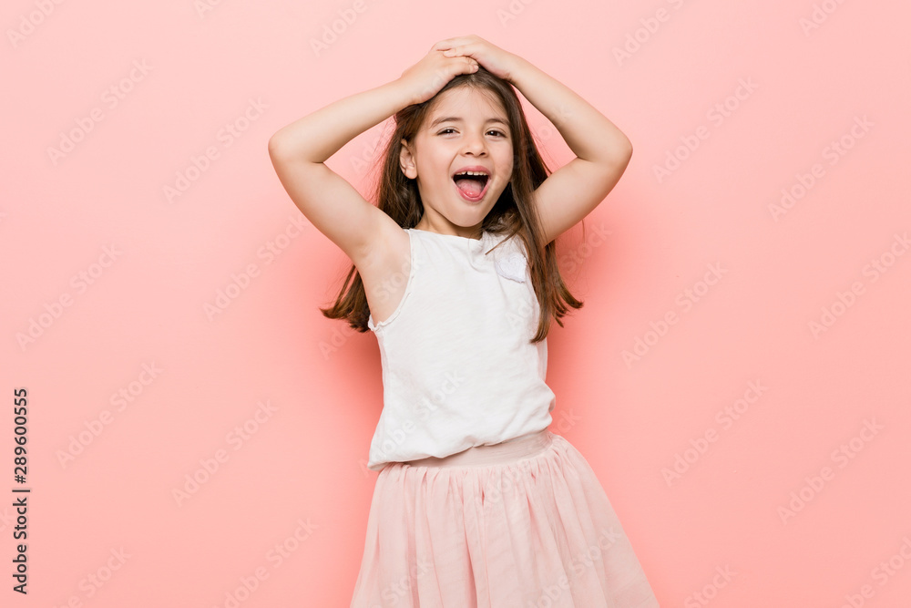Little girl wearing a princess look laughs joyfully keeping hands on head. Happiness concept. Little girl wearing a princess look laughs joyfully keeping hands on head. Happiness concept.