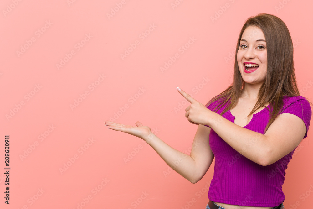 Young hispanic woman against a pink wall excited holding a copy space on palm. Young hispanic woman against a pink wall excited holding a copy space on palm.