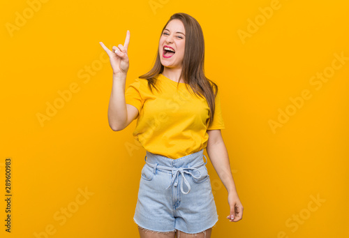Young woman teenager wearing a yellow shirt showing a horns gesture as a revolution concept.