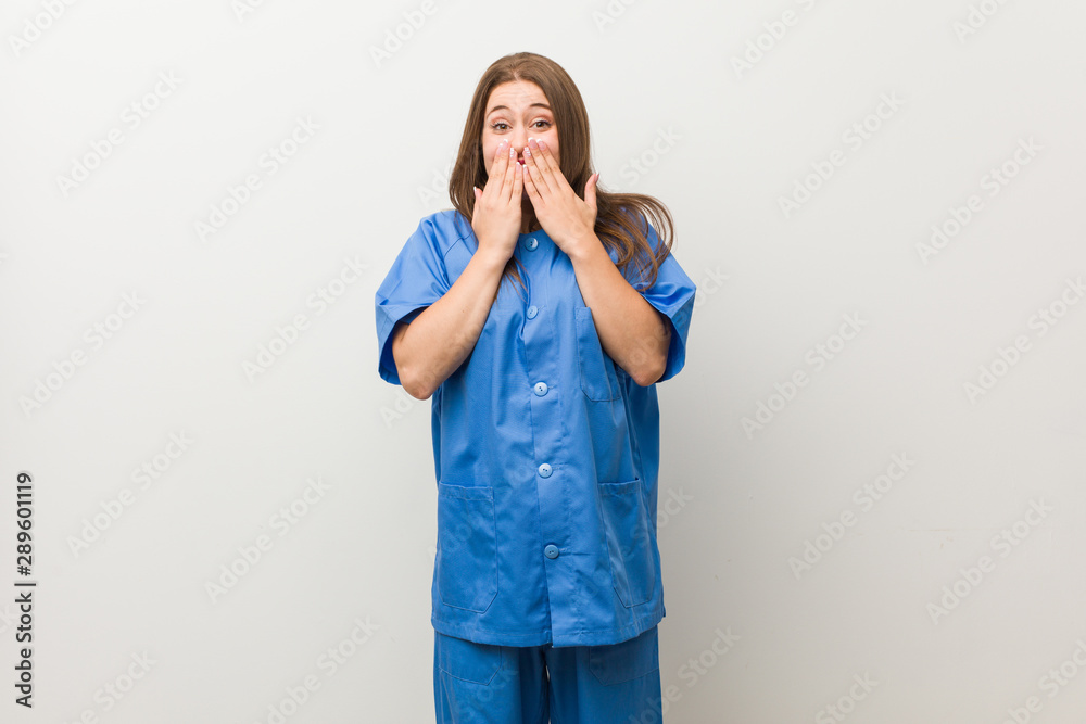 Young nurse woman against a white wall laughing about something, covering mouth with hands. Young nurse woman against a white wall laughing about something, covering mouth with hands.