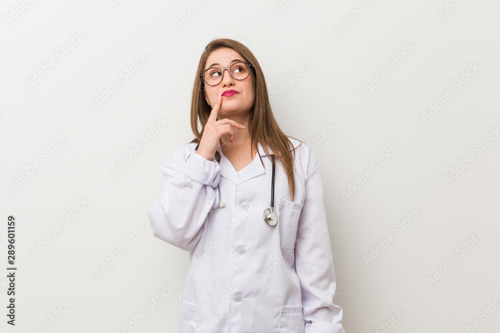 Young doctor woman against a white wall looking sideways with doubtful and skeptical expression. Young doctor woman against a white wall looking sideways with doubtful and skeptical expression.