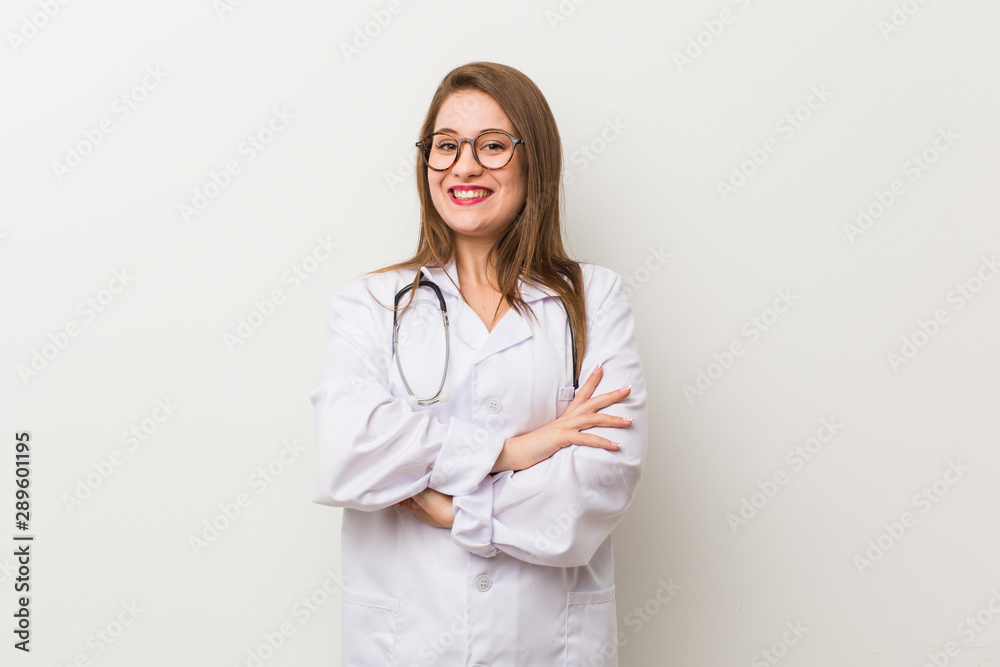 Young doctor woman against a white wall who feels confident, crossing arms with determination. Young doctor woman against a white wall who feels confident, crossing arms with determination.