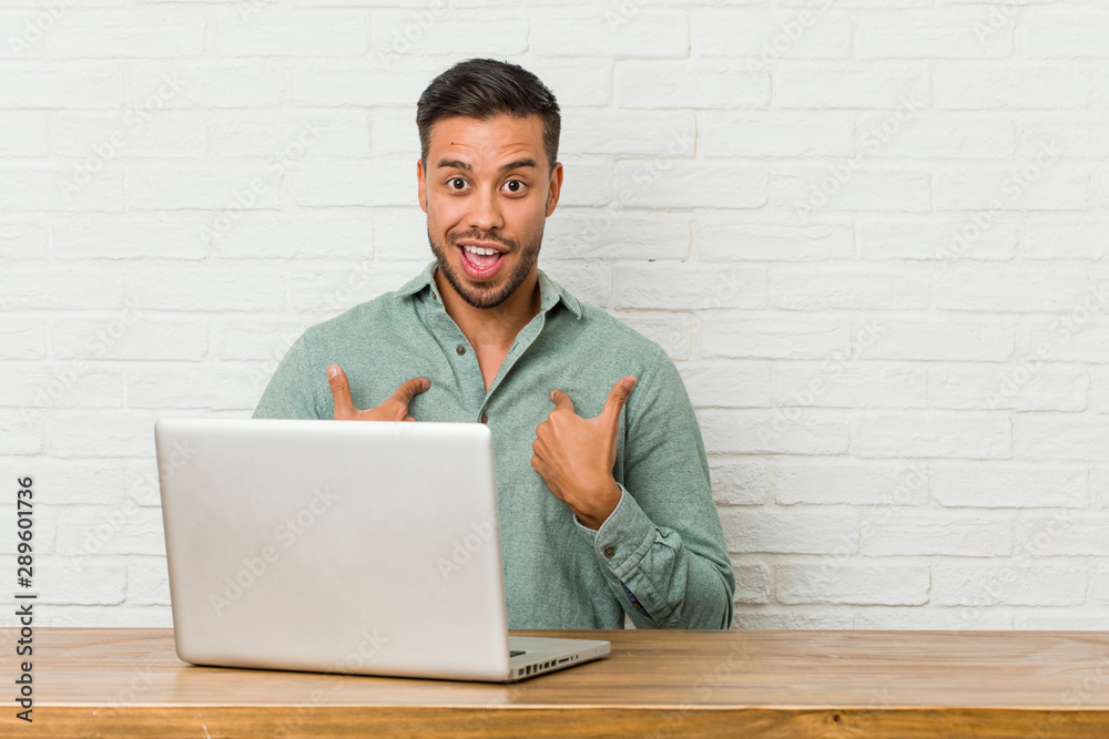 Young filipino man sitting working with his laptop surprised pointing with finger, smiling broadly. Young filipino man sitting working with his laptop surprised pointing with finger, smiling broadly.