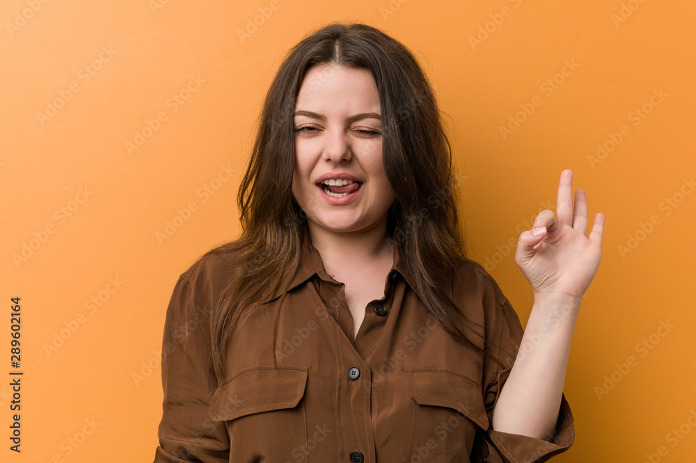 Young curvy russian woman winks an eye and holds an okay gesture with hand. Young curvy russian woman winks an eye and holds an okay gesture with hand.