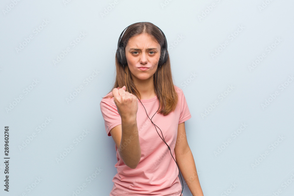 Young pretty caucasian woman showing fist to front, angry expression. She is listening to music with headphones. Young pretty caucasian woman showing fist to front, angry expression. She is listening to music with headphones.