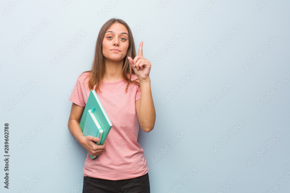 Young pretty caucasian woman showing number one. She is holding books. Young pretty caucasian woman showing number one. She is holding books.