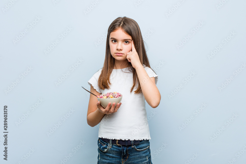 Little caucasian girl holding a cereal bowl pointing his temple with finger, thinking, focused on a task. Little caucasian girl holding a cereal bowl pointing his temple with finger, thinking, focused on a task.