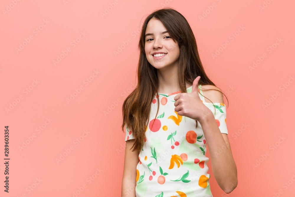 Girl wearing a summer clothes against a red wall smiling and raising thumb up Girl wearing a summer clothes against a red wall smiling and raising thumb up