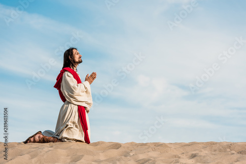man praying on knees in desert on golden sand