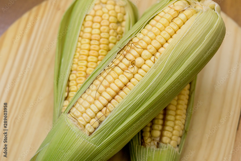 Closeup of raw corn cobs with straw over wood Closeup of raw corn cobs with straw over wood