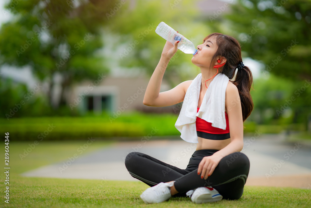 Asian attractive sporty woman in red dress drinking water from a bottle after jogging or running while she sitting in park.. Asian attractive sporty woman in red dress drinking water from a bottle after jogging or running while she sitting in park..