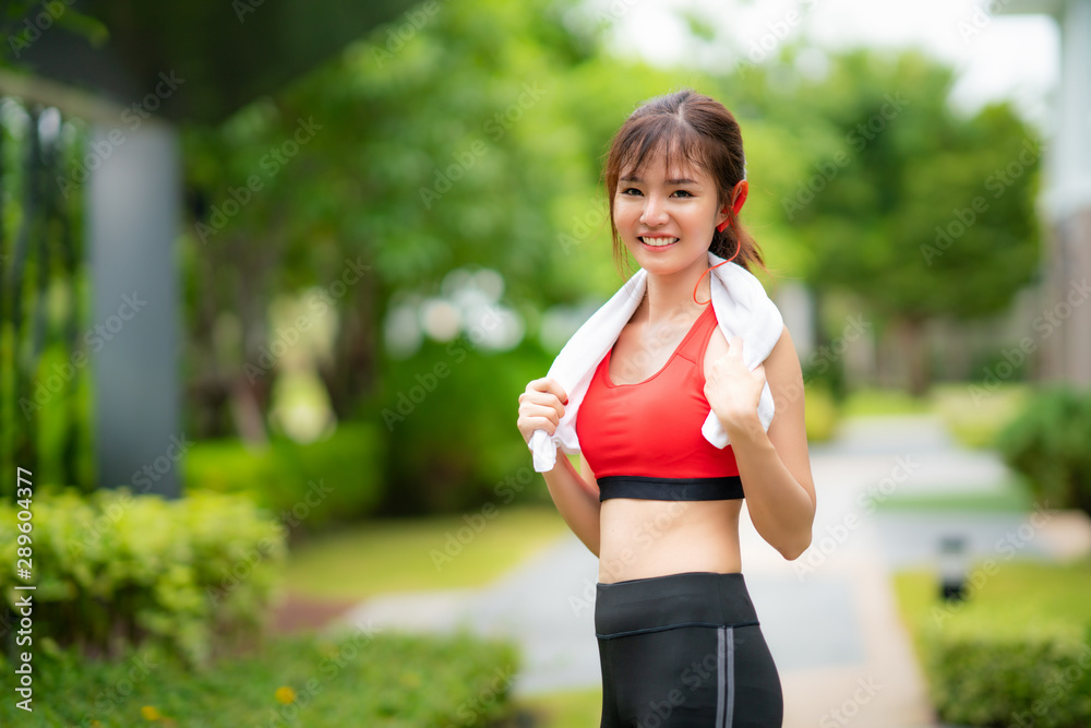 Asian young woman dressed in a red stands smiling, while relaxing after a workout in the village in the morning Asian young woman dressed in a red stands smiling, while relaxing after a workout in the village in the morning
