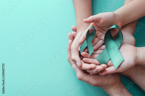 Adult and children hands holding Teal ribbons on blue background, Ovarian Cancer, cervical Cancer, anti bullying and sexual assault awareness photo