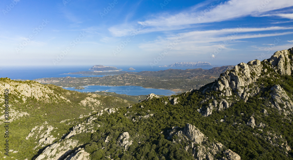 View from above, panoramic view of some stunning granite mountains illuminated by sunset. Beautiful bay with turquoise sea in the background. San Pantaleo, Sardinia, Italy.