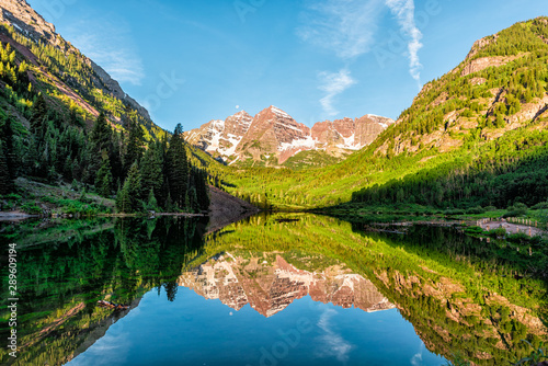 Maroon Bells lake at sunrise panoramic view in Aspen, Colorado with rocky mountain peak and snow in July 2019 summer and vibrant light reflection on water