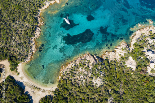 View from above, stunning aerial view of a sailboat floating on a beautiful turquoise sea that bathes the green and rocky coasts of Sardinia. Emerald Coast (Costa Smeralda) Italy