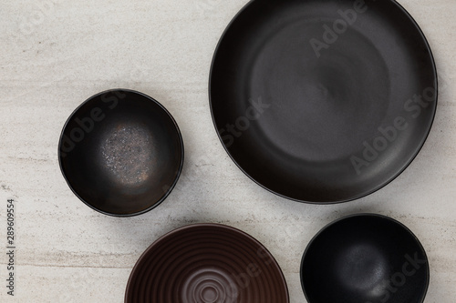 Group of empty blank black ceramic round bowls and plates on white stone blackground, Top view of traditional handcrafted kitchenware concept