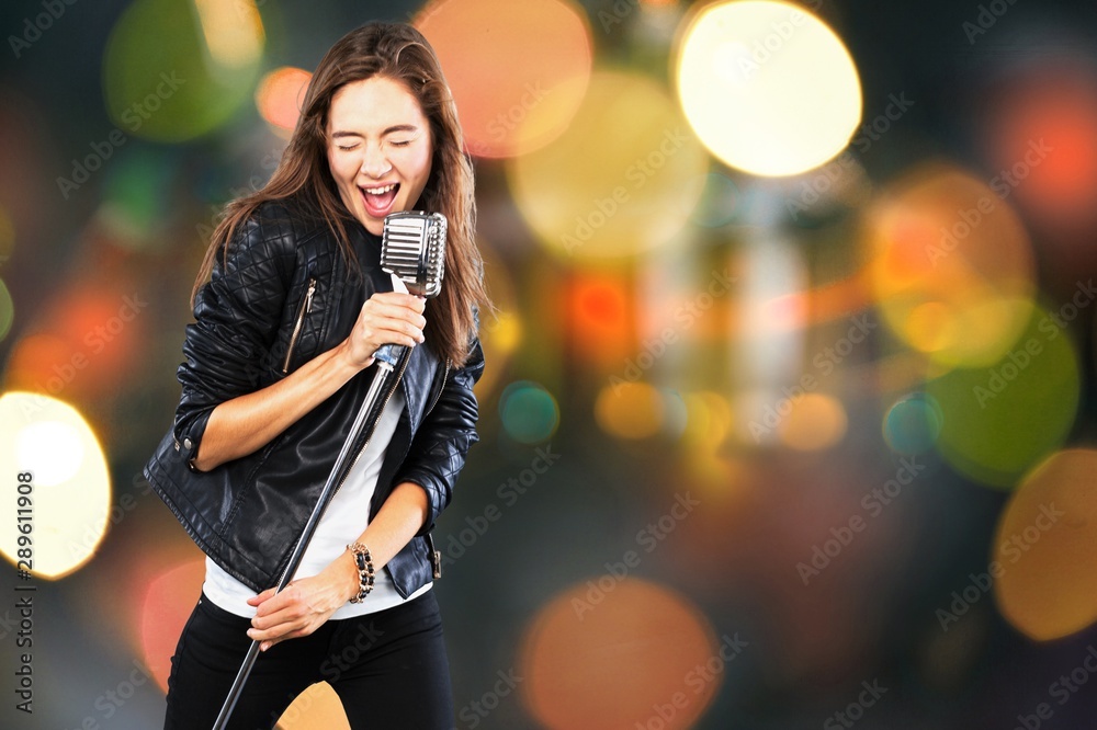 Young woman singing with microphone on blurred background Young woman singing with microphone on blurred background