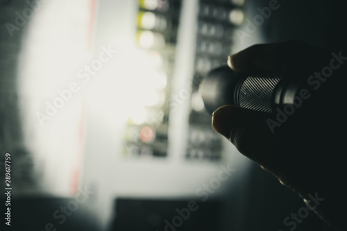 photo during a power outage with silhouette of hand holding a flashlight aimed at a fuse box photo