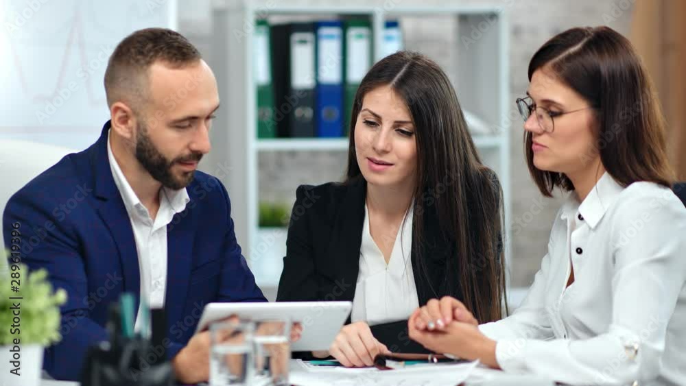 Two smiling female employee showing marketing researching data to male boss using tablet pc Two smiling female employee showing marketing researching data to male boss using tablet pc