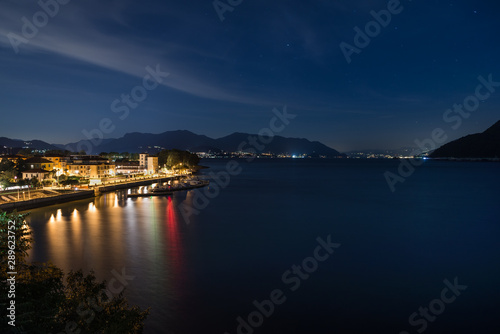 Famous big European lake at night. Lake Maggiore with the city of Maccagno, in the background the lights of the stretch of coast between the cities of Germignaga and Stresa, Italy © AleMasche72