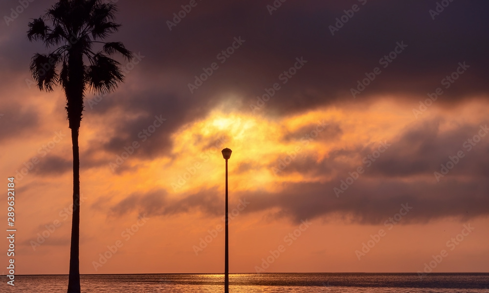 Palm tree and street lamp, heavy dramatic clouds and bright sky. Beautiful African sunset over the lagoon. Palm tree and street lamp, heavy dramatic clouds and bright sky. Beautiful African sunset over the lagoon.