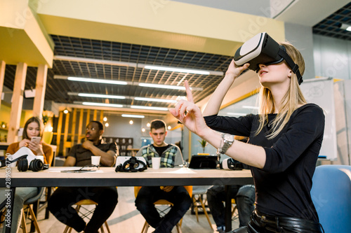 Creative business team using virtual reality glasses at the office. Young girl wearing 3d vr headset, her colleagues sitting at the table. Teamwork, startup, innovation concept