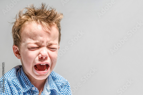 Crying little boy on a gray background .
