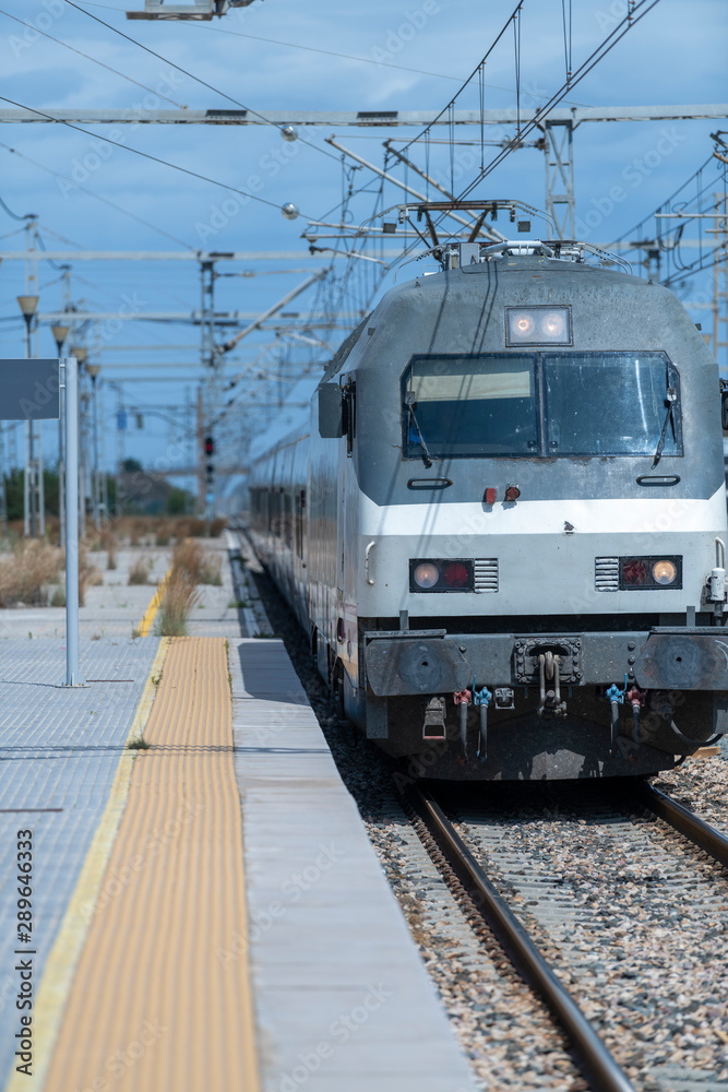 A grey and white train with wire fences and blue sky with white background clouds.