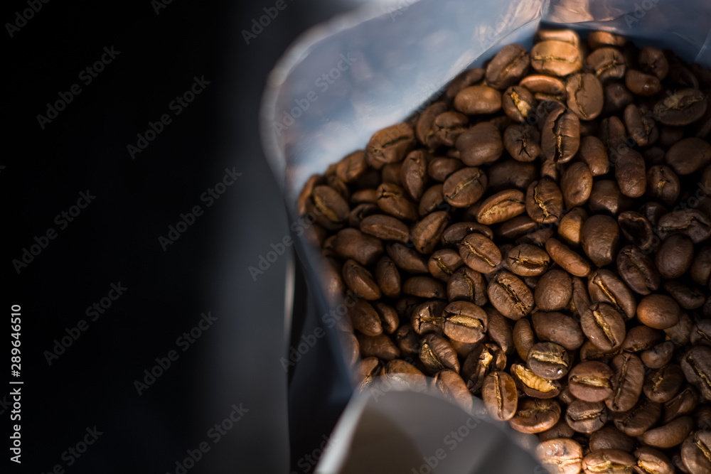 Lots of coffee beans in a bag on dark background. Arabica. Coffee shop.