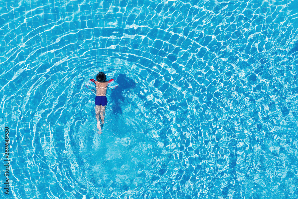 Top view of a boy swimming in an outdoor pool. Clear water.