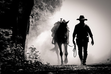 Foto auf Leinwand Pferde Schwarz-Weiß-Bild Silhouette des Cowboys und des Pferdes bei Sonnenaufgang am Morgen  © subinpumsom