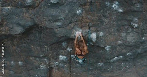 Aerial drone view of young fit woman lead rock climbing on an outdoors sport route, fast experienced rock climber