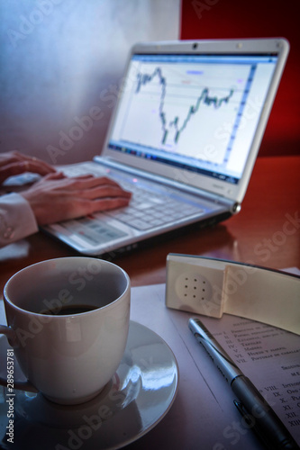 Close-up of female hands making notes in the laptop at office hile taking a cup of coffee photo