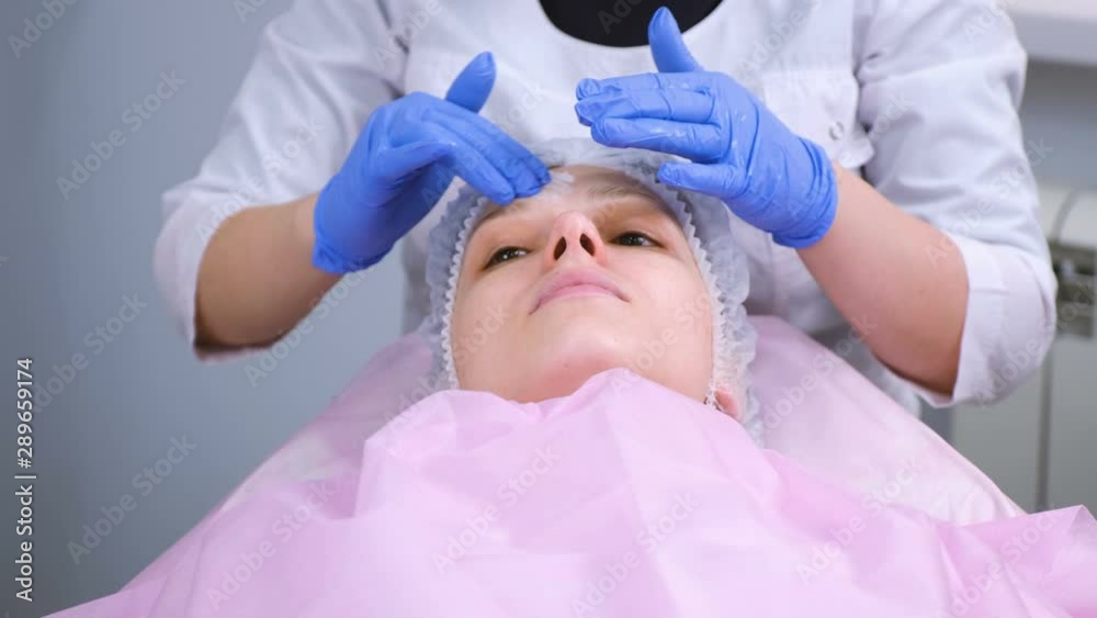 Beautician puts mask on woman's face. Preparing for a cleaning face