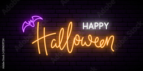 Happy Halloween neon sign board. Bright light inscription on brick wall background.
