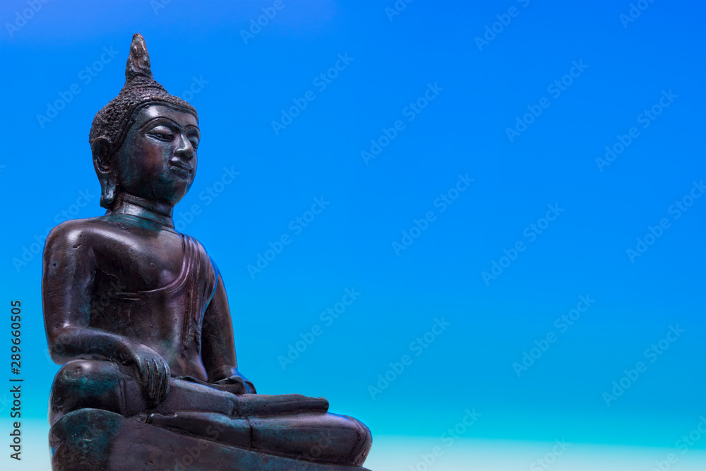Statue of Buddha sitting in meditation with blue space Statue of Buddha sitting in meditation with blue space