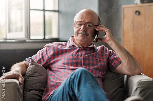 Retired hispanic man talking on phone sitting at living room. Discuss important questions.
